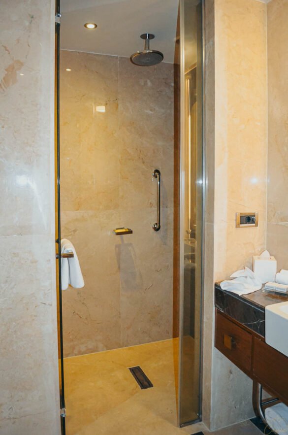 Box de chuveiro moderno com revestimento em pedra clara e ducha de teto.