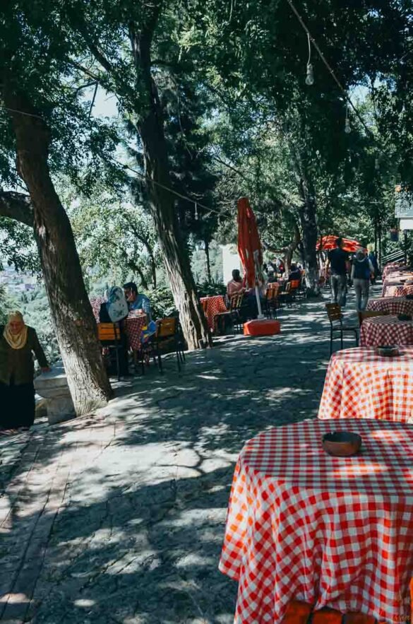 Mesas redondas com toalhas xadrez vermelhas em café ao ar livre sob árvores em Istambul.