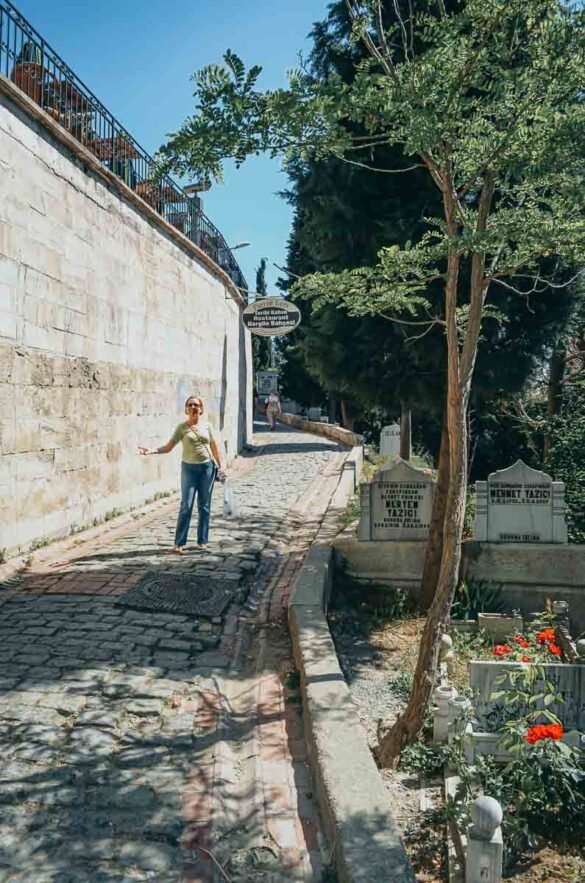 Mulher caminha por trilha de pedras cercada por árvores e lápides antigas em Eyüp, Istambul.