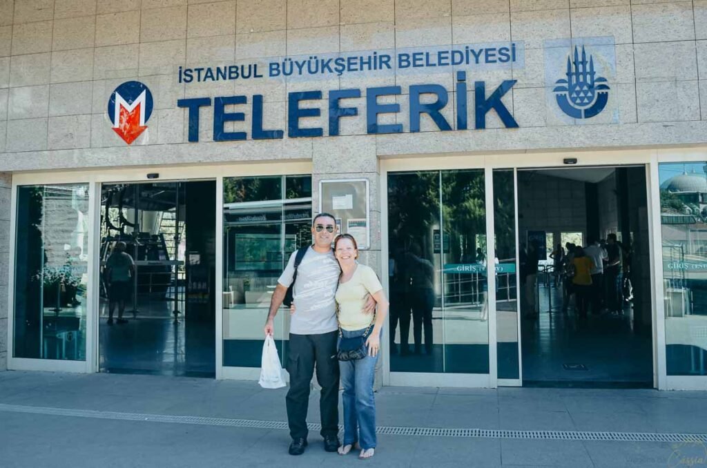 Casal de turistas abraçados em frente à entrada da estação de teleférico (Teleferik) em Istambul.