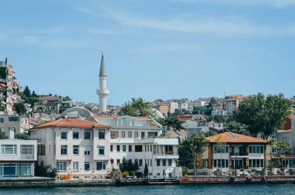 Casas brancas de teto laranja e um minarete branco à beira do Estreito de Bósforo na Turquia.