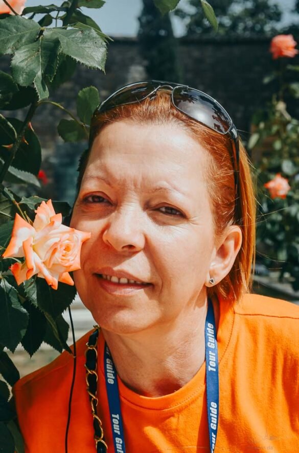 Close do rosto de uma mulher sorrindo ao lado de uma rosa em tons de pêssego e laranja.