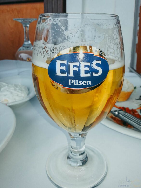 Close-up de um copo tulipa de cerveja Efes Pilsen com espuma sobre mesa de restaurante.