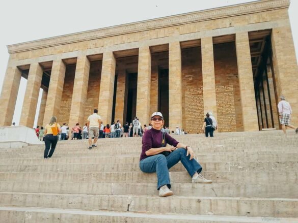 escadarias-hall-honra-mausoleu-ataturk Mulher sentada nas escadarias do mausoléu de Atatürk diante de colunas gigantescas.