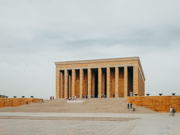 fachada-mausoleu-ataturk-escadaria-ankara Fachada imponente do Mausoléu de Atatürk com grandes colunas verticais e escadaria larga.