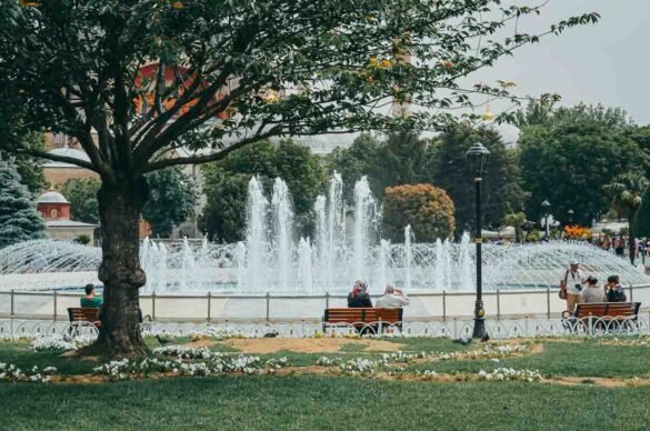 Fonte jorrando água em parque arborizado com bancos e pessoas ao fundo em Istambul.