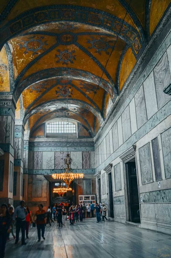 Corredor amplo com teto abobadado decorado em dourado e lustres baixos na Hagia Sophia.