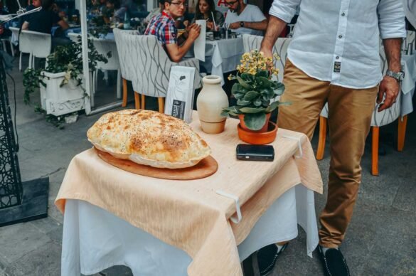 Pão turco grande e dourado exposto em uma mesa pequena na calçada de um restaurante.