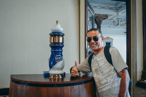 Homem sorridente fazendo sinal de positivo ao lado de uma chopeira da marca turca Efes.