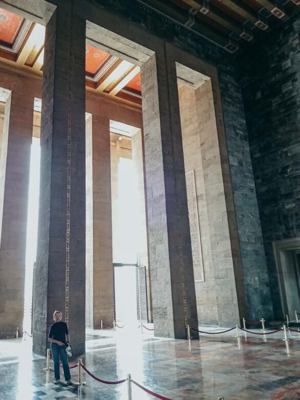 interior-colunas-gigantes-mausoleu-anitkabir Pessoa em pé ao lado de coluna gigante de mármore, mostrando a escala monumental do interior.