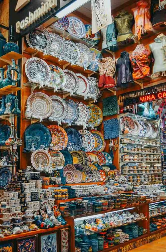 Prateleiras repletas de pratos, xícaras e pashminas coloridas em uma loja no Grand Bazaar.