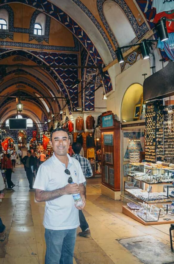 Homem em primeiro plano em corredor do bazar com tetos decorados e lojas de joias ao fundo.