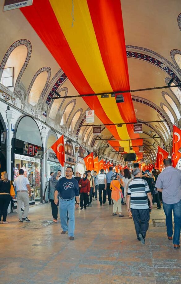 Corredor interno do Grande Bazar com teto arqueado e grandes bandeiras da Turquia penduradas.