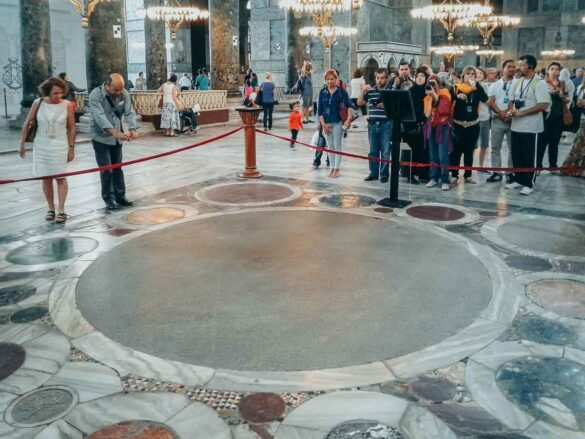 Círculos de mármore coloridos no chão de pedra da Basílica de Santa Sofia, cercados por cordão vermelho.