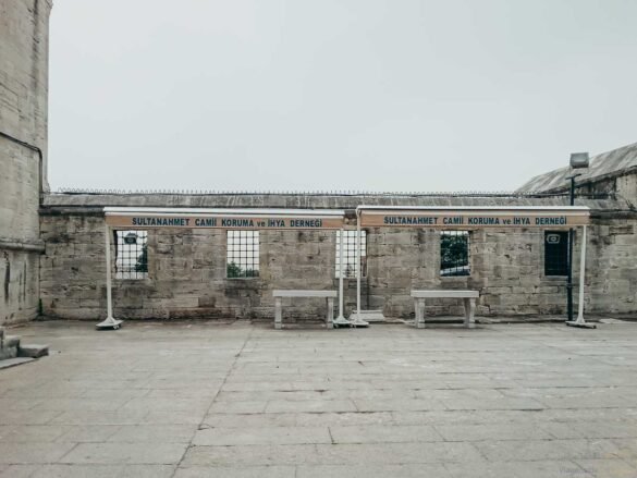 Pátio de pedra da Mesquita Azul com placas de associação e janelas com grades de ferro.