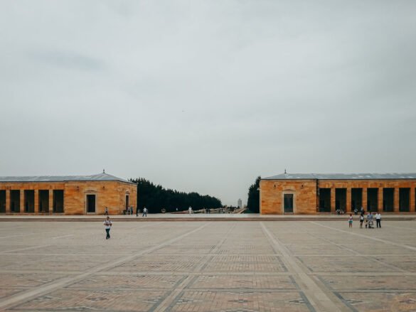 praca-cerimonial-anitkabir-ankara-turquia-1 Vasta praça pavimentada com edifícios de pedra simétricos sob céu nublado no Anıtkabir.