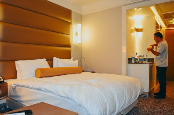 Cama de casal grande com cabeceira estofada em tons de marrom e iluminação quente.