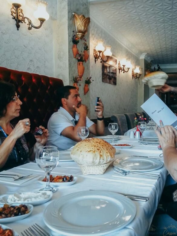 Interior de restaurante elegante com pessoas sentadas à mesa e pães turcos inflados em destaque.