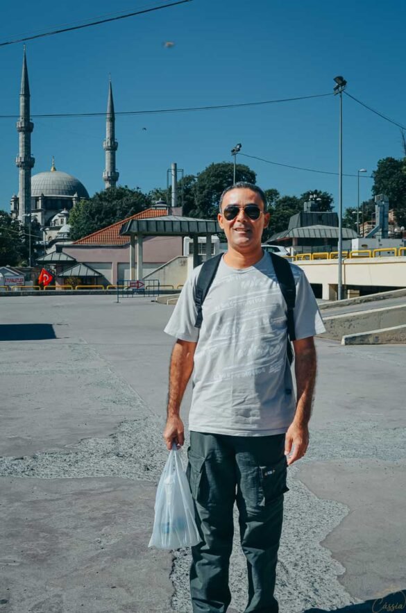 Homem de óculos escuros e mochila posando em frente a uma mesquita histórica com minaretes na Turquia.