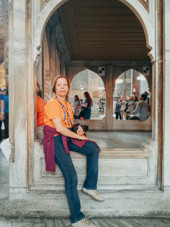 Mulher sentada em arco de mármore dentro da Hagia Sophia com câmera fotográfica nas mãos.