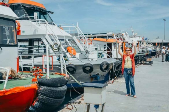Mulher com braços levantados em um pier ao lado de vários barcos de passeio.