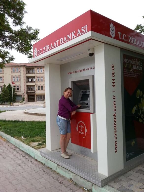 Mulher sorridente em frente a um caixa eletrônico vermelho e branco do Ziraat Bankasi na Turquia.