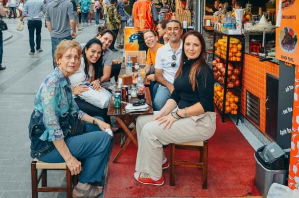Grupo de turistas sorridentes sentados em mesas pequenas em uma calçada de Istambul.