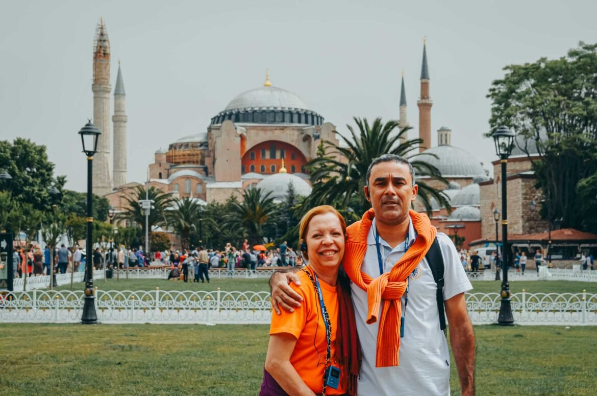 Casal sorrindo abraçado com a Basílica de Santa Sofia ao fundo em Istambul.