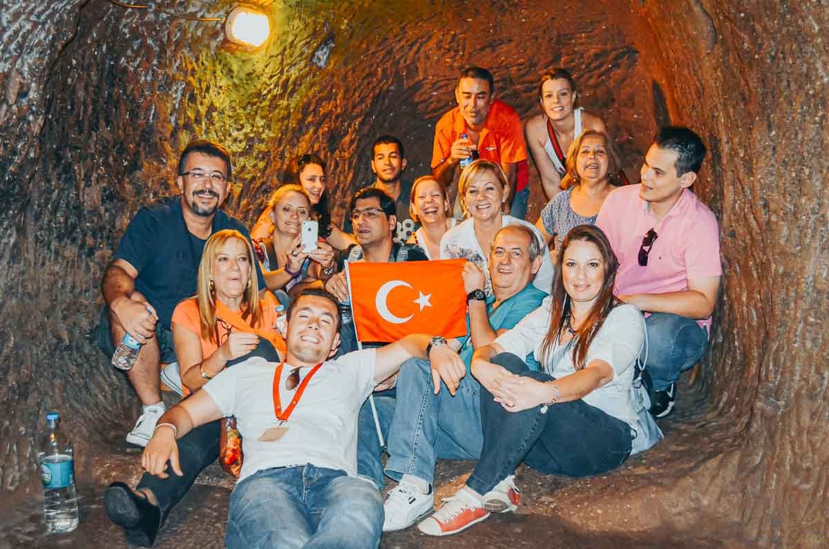 grupo-turistas-bandeira-turquia-caverna Grupo de pessoas posando com a bandeira da Turquia dentro de uma caverna.