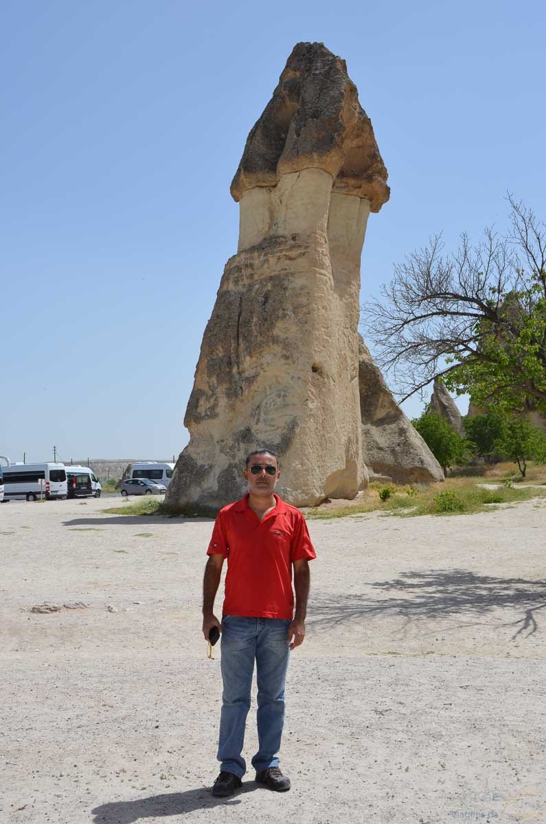 homem-chamine-fada-gigante-capadocia Homem de camisa vermelha em frente a uma enorme formação rochosa de chaminé de fada.