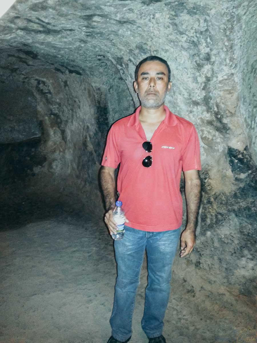 homem-tunel-cidade-subterranea-capadocia Homem de camisa vermelha em um túnel de pedra de uma cidade subterrânea.