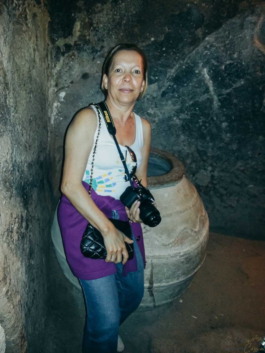 mulher-jarro-antigo-caverna-turquia Mulher com câmera ao lado de um grande jarro de barro antigo em uma caverna.