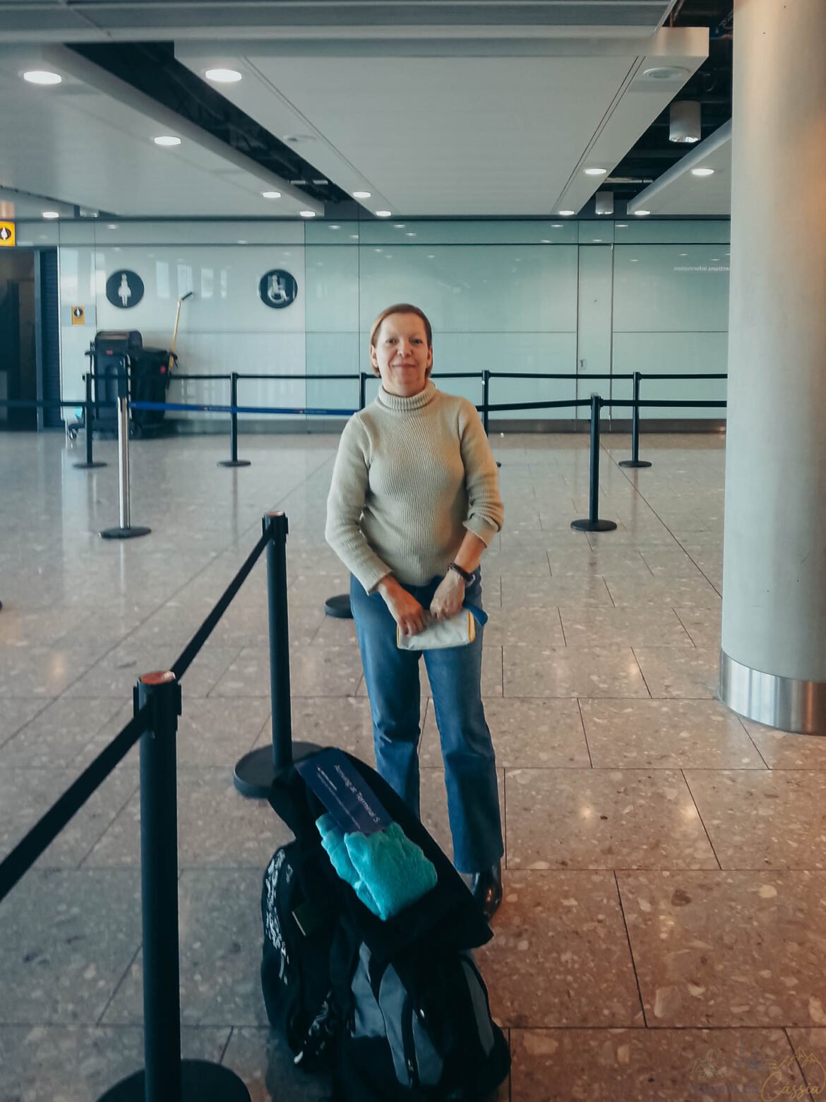 Mulher em pé em um saguão de aeroporto ao lado de sua bagagem na fila de embarque.