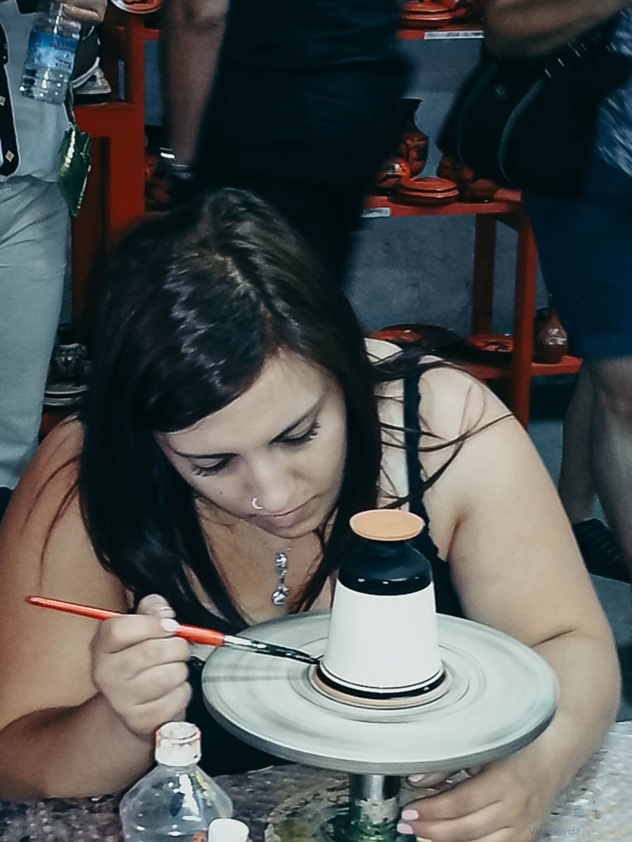 mulher-pintando-ceramica-artesanal Mulher pintando com pincel os detalhes de um pequeno vaso de cerâmica.