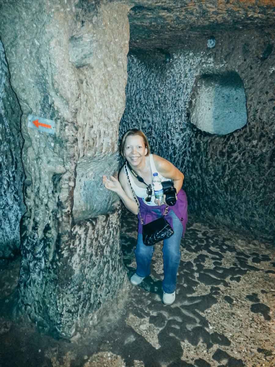 mulher-sinalizacao-vermelha-cidade-subterranea Mulher sorrindo perto de uma seta vermelha pintada na parede de pedra.