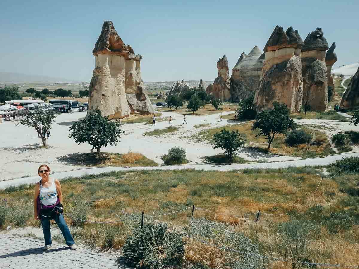 mulher-trilha-vale-formacoes-capadocia Mulher sorrindo em uma trilha com vista para um vale de chaminés de fada.
