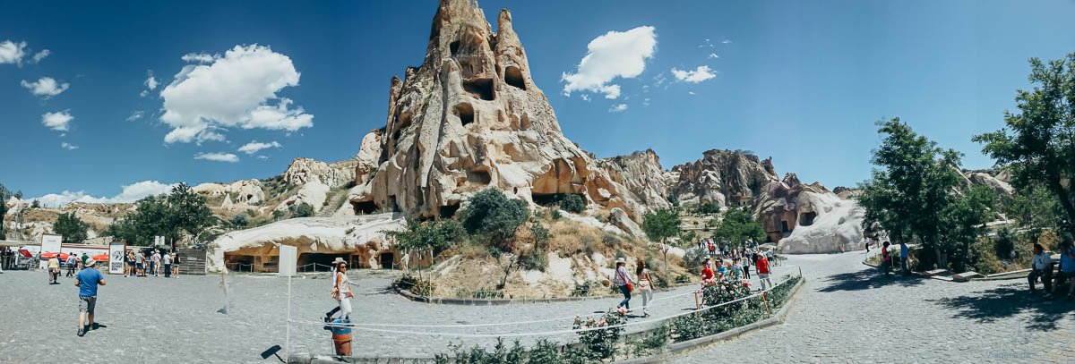 museu-ao-ar-livre-goreme-capadocia-panoramica Vista panorâmica de formação rochosa histórica com turistas na Capadócia.