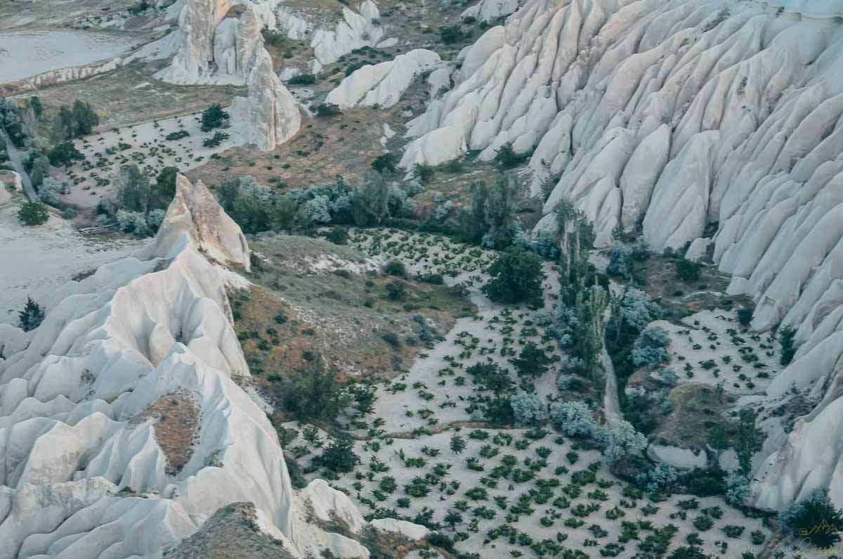 plantacoes-entre-rochas-brancas-capadocia Vista aérea de pequenas plantações verdes cultivadas entre imponentes formações rochosas brancas e esculpidas na Capadócia.