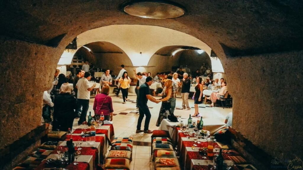 Visão ampla de turistas dançando em um salão de restaurante escavado na caverna na Capadócia.