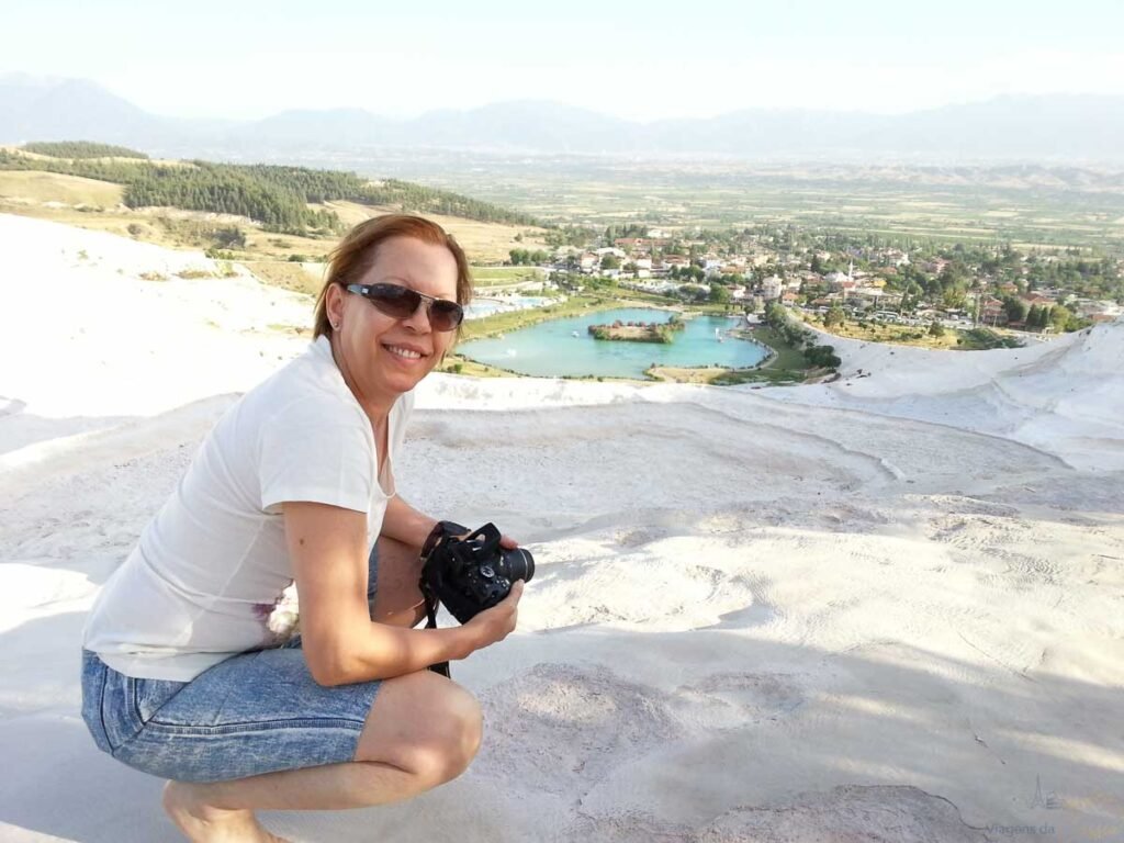Mulher agachada na superfície branca de travertino sorrindo para a câmera com óculos de sol.