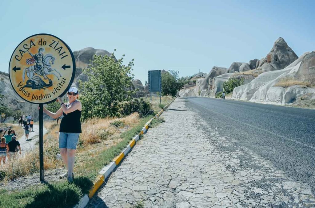 Mulher com placa turística indicando a Casa do Ziah nas paisagens da Capadócia.