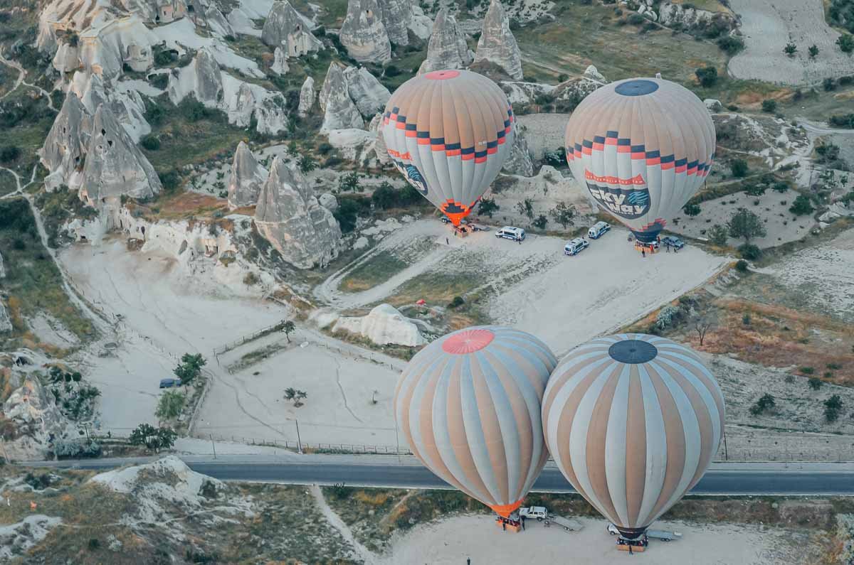 vista-aerea-baloes-chao-capadocia Vista aérea de balões de ar quente coloridos pousados no solo rochoso.