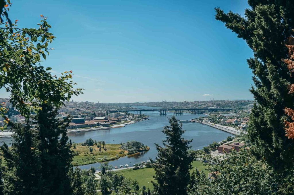 Vista do rio Chifre de Ouro emoldurada por árvores e pontes ao fundo sob céu limpo.