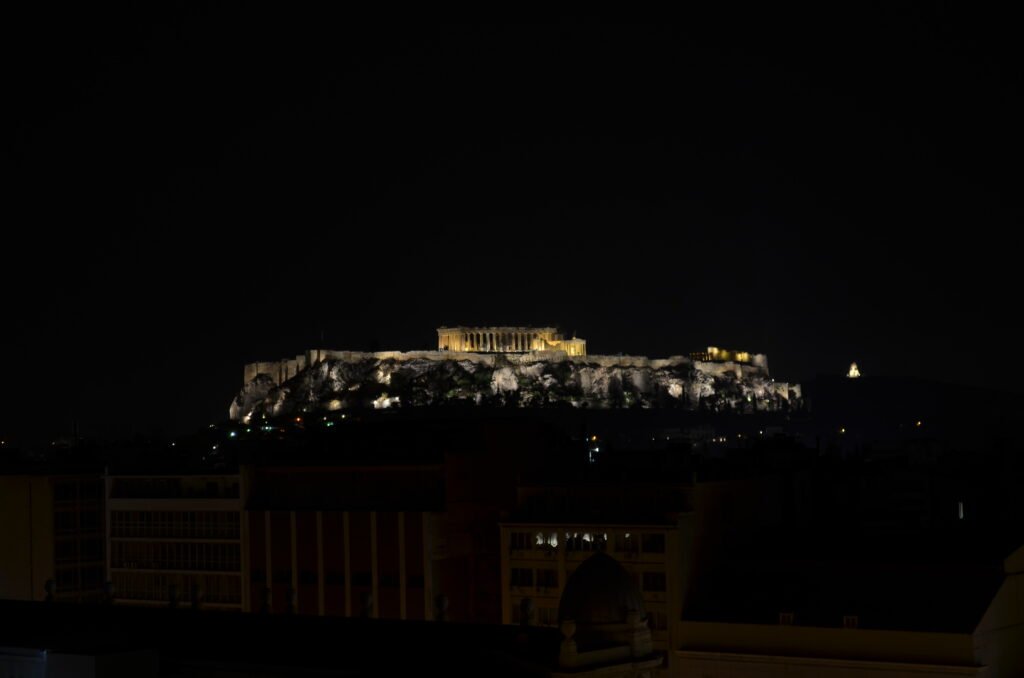 Acrópole de Atenas e Parthenon iluminados no topo da colina durante a noite escura.
