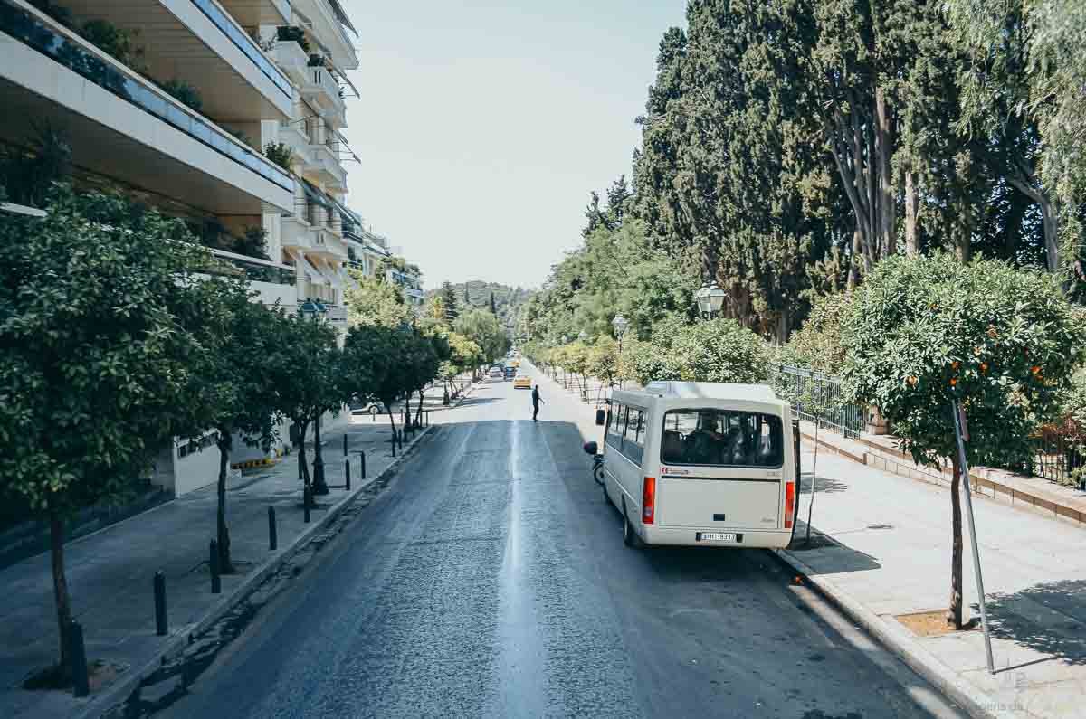 avenida-arborizada-minibus-atenas-grécia Avenida larga arborizada com minibus branco estacionado e árvores alinhadas.