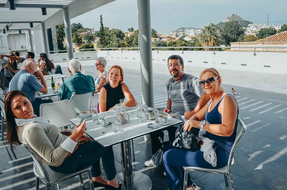 cafe-terraco-museu-acropole-atenas Grupo de pessoas reunido ao redor da mesa no café ao ar livre do Museu da Acrópole.