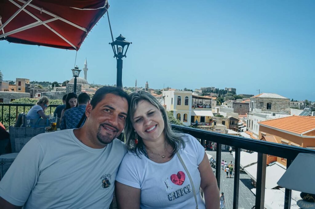 Casal sorrindo em terraço com vista para minarete e telhados antigos.