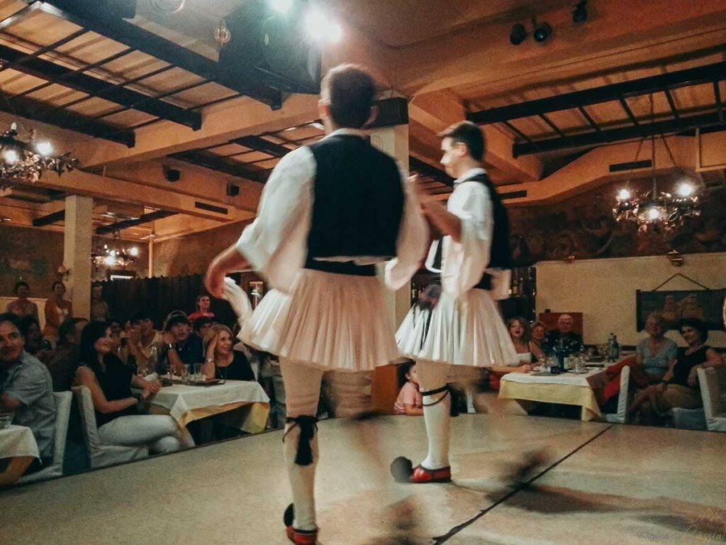 Dançarinos com trajes tradicionais foustanella apresentando dança folclórica grega em restaurante.
