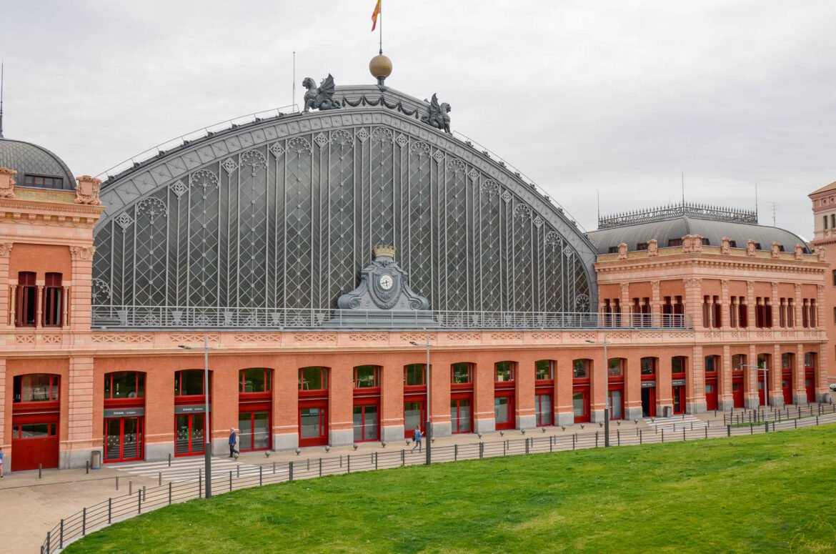 Fachada monumental em arco de ferro e vidro da estação de trem de Atocha em Madri.