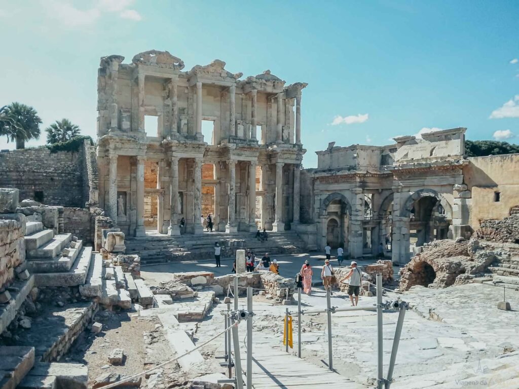 Fachada de dois andares da Biblioteca de Celso com colunas de mármore e turistas na praça.